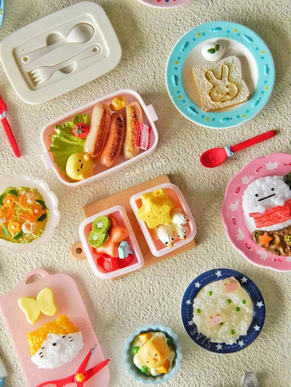 A collection of miniature food items and a pink plastic lunch box with a handle on a light textured surface.