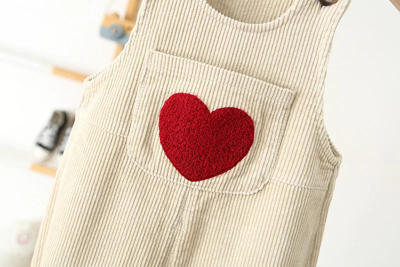 A beige corduroy toddler overalls featuring a red felt heart embroidery patch on the chest pocket.