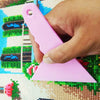 A hand holds a pink diamond painting precision tool against a colorful fabric background.