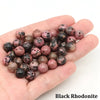 A handful of black rhodonite round beads for jewelry making resting in a person's palm.