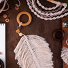 A close-up of natural wooden spacer beads, feathers, and twine arranged on a dark wooden surface for jewelry making.