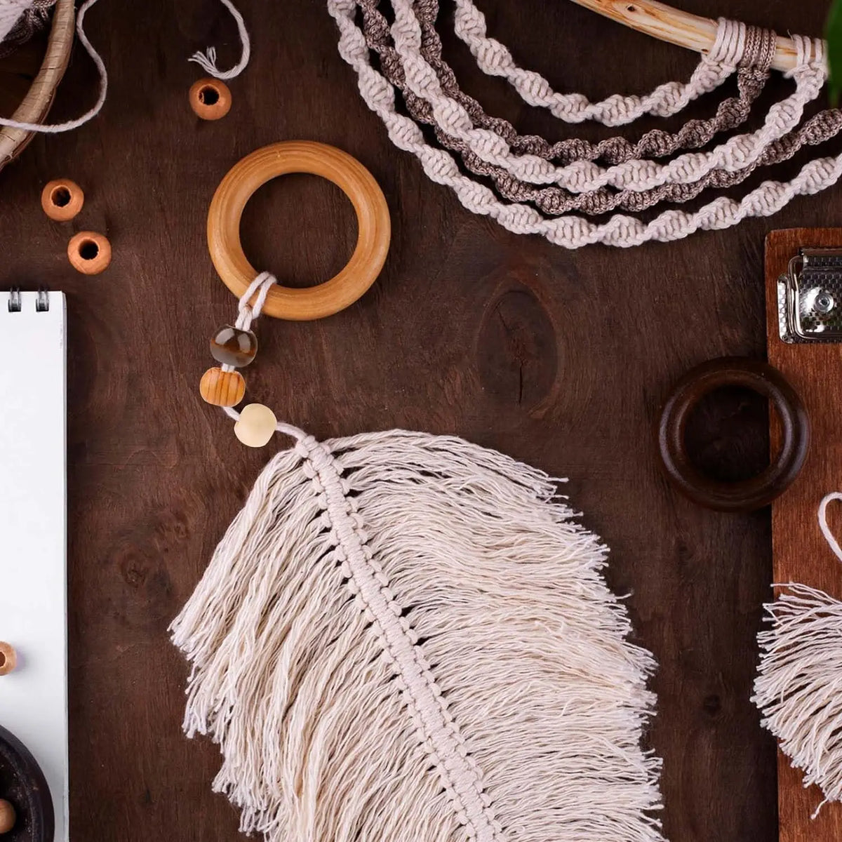 A close-up of natural wooden spacer beads, feathers, and twine arranged on a dark wooden surface for jewelry making.