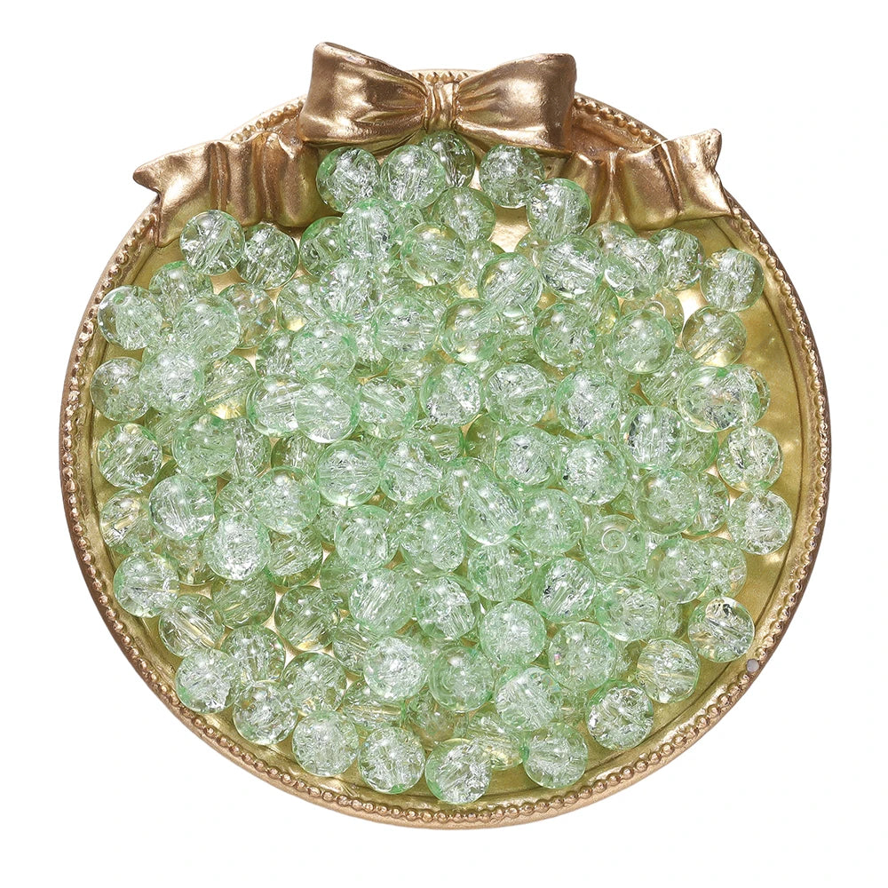 A round gold-rimmed dish filled with small, light green glass crackle beads for jewelry making.
