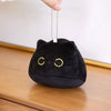 A round black cat plush keychain with yellow eyes is being held by a hand.
