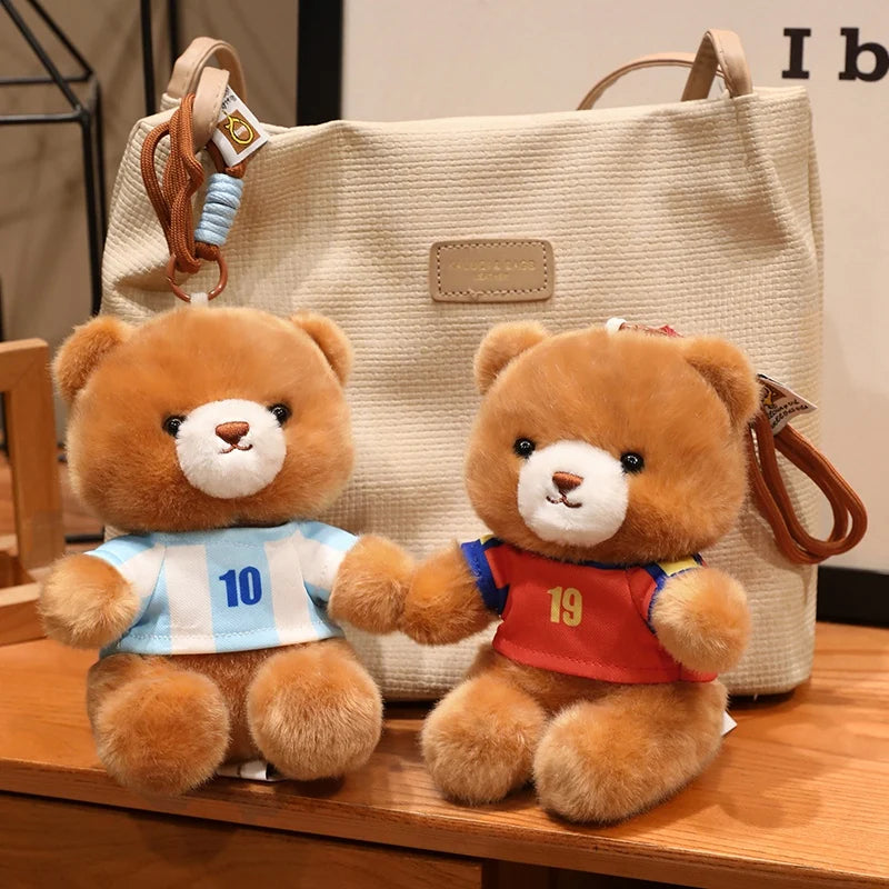 Two teddy bears wearing football jerseys, one blue and white, and the other red, sitting in front of a beige tote bag.
