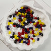 A variety of oval glass rice grain beads in red, yellow, white, black, and blue are displayed in a white dish.