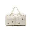 A cream-colored diaper bag with a light quilted pattern and bear embroidery.