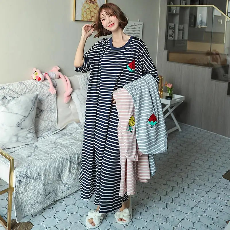 A woman wearing a navy and white striped lounge dress with colorful floral embroidery sits on a sofa.