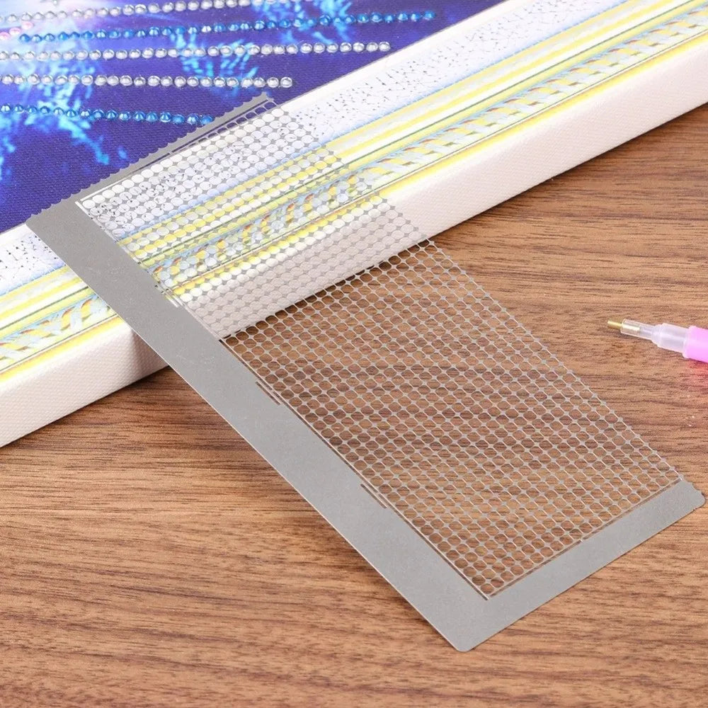 A stainless steel cross ruler used for diamond painting is shown resting on a wooden surface.