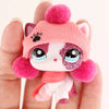 A small pink knitted animal figure resembling a cat with pink and white fur and large sparkly eyes is held in a hand.