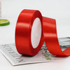 A roll of red satin ribbon for gift wrapping and crafts lying on a white surface.