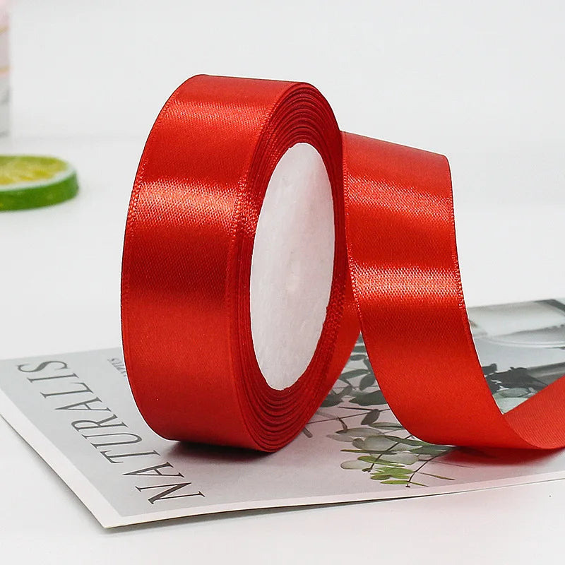 A roll of red satin ribbon for gift wrapping and crafts lying on a white surface.