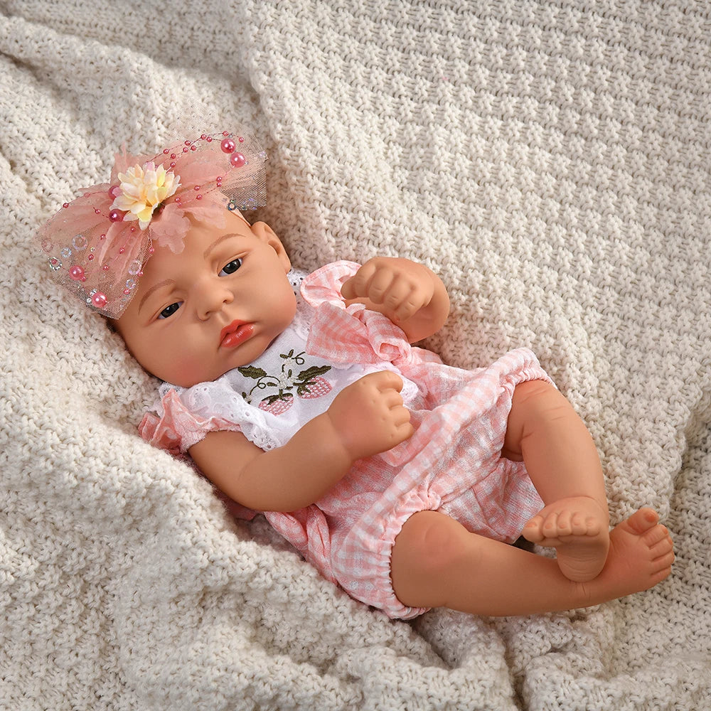 A lifelike vinyl reborn doll with a pink floral headband and a pink gingham outfit lying on a cream knitted fabric.