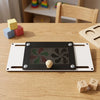 A black wooden sensory activity board with gears and a knob rests on a light wood table next to colorful wooden blocks.