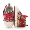 A pair of leopard print soft sole baby sneakers with pink laces and red bows.