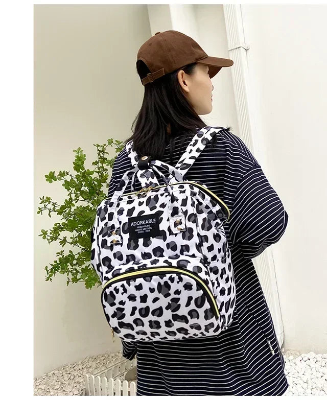 A woman wearing a striped shirt holds a black and white cartoon print waterproof diaper bag.