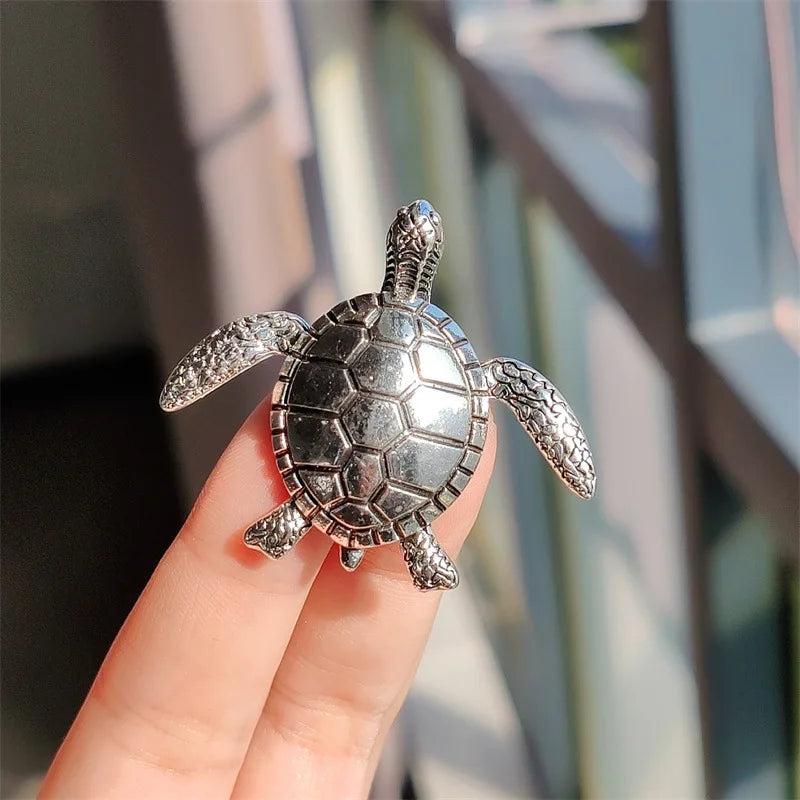 Silver rhinestone turtle brooch pin held in a hand against a blurred background.