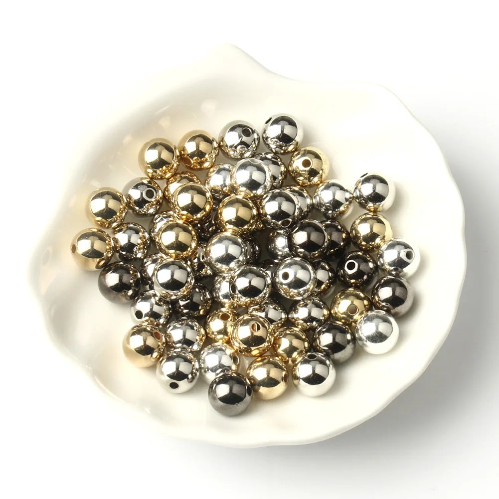 A pile of round spacer beads in gold and silver tones resting in a white dish.