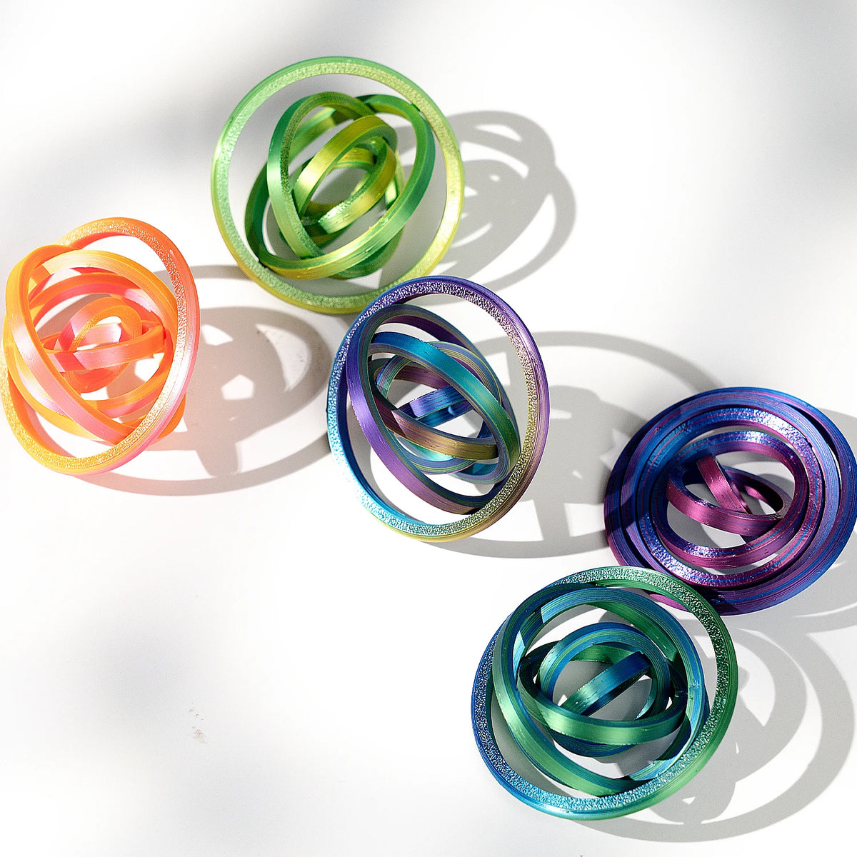 A collection of colorful, spiraled rings or spinners in various shades of green, orange, and purple, casting shadows on a whi