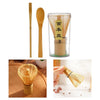 A set of traditional bamboo matcha whisks, including a long stick and a bowl-shaped whisk, displayed in a clear glass contain