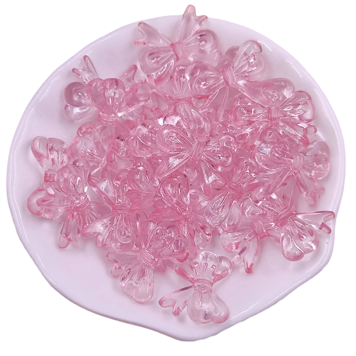 A pile of pink acrylic bow beads for jewelry making arranged on a white oval dish.