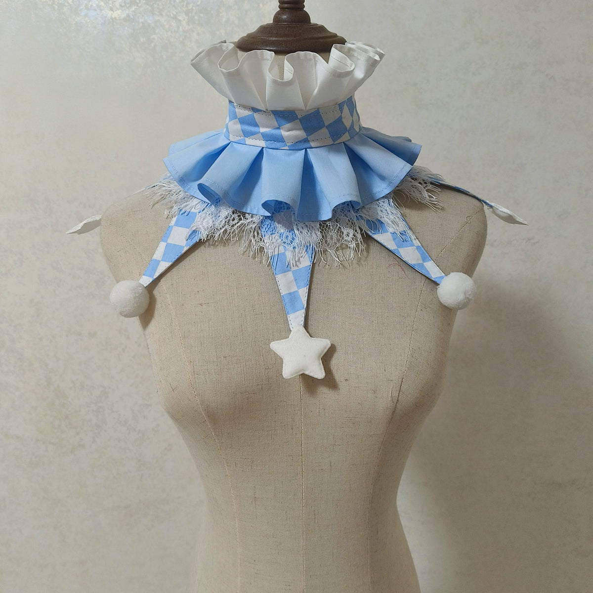 A handmade clown ruff collar featuring blue and white checkered fabric, tulle, and white pom-poms on a mannequin.
