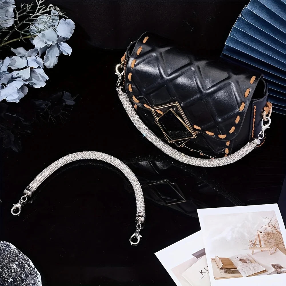 A black faux leather purse with gold stitching and a sparkling rhinestone strap is displayed on a dark surface.