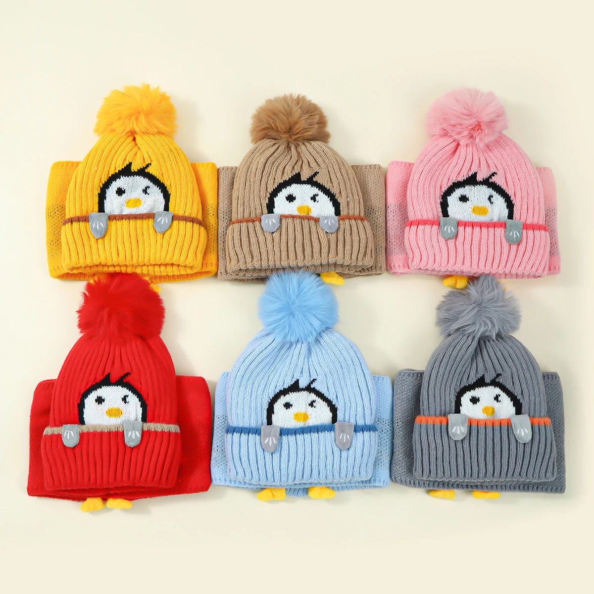 A set of colorful knit penguin hats and scarves in yellow, beige, pink, and blue.
