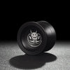 A black professional aluminum alloy yo-yo with a white and black design resting on a textured surface.