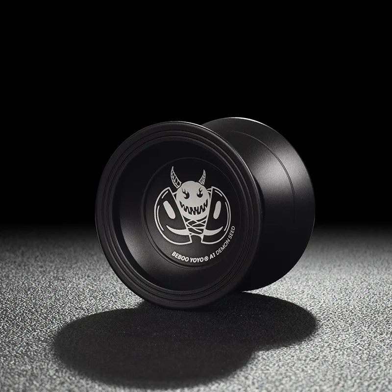 A black professional aluminum alloy yo-yo with a white and black design resting on a textured surface.