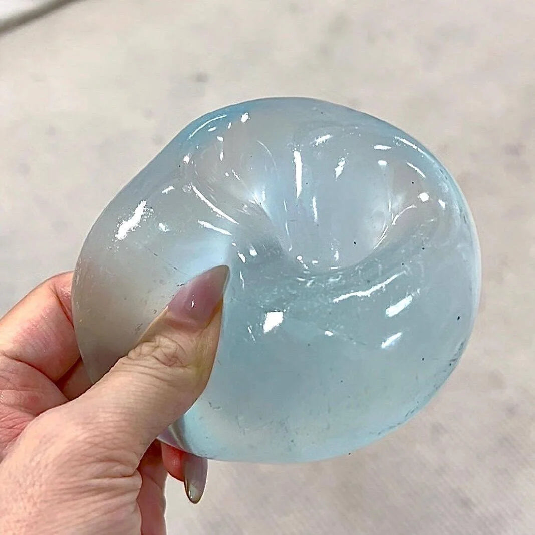 A hand holds a translucent blue coconut oil squishy stress relief ball.
