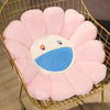 A large pink sunflower plush cushion with a white center and blue mouth is displayed in a gold wire basket.