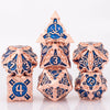 A set of seven metal dice featuring a skull and dragon design in rose gold and blue enamel.