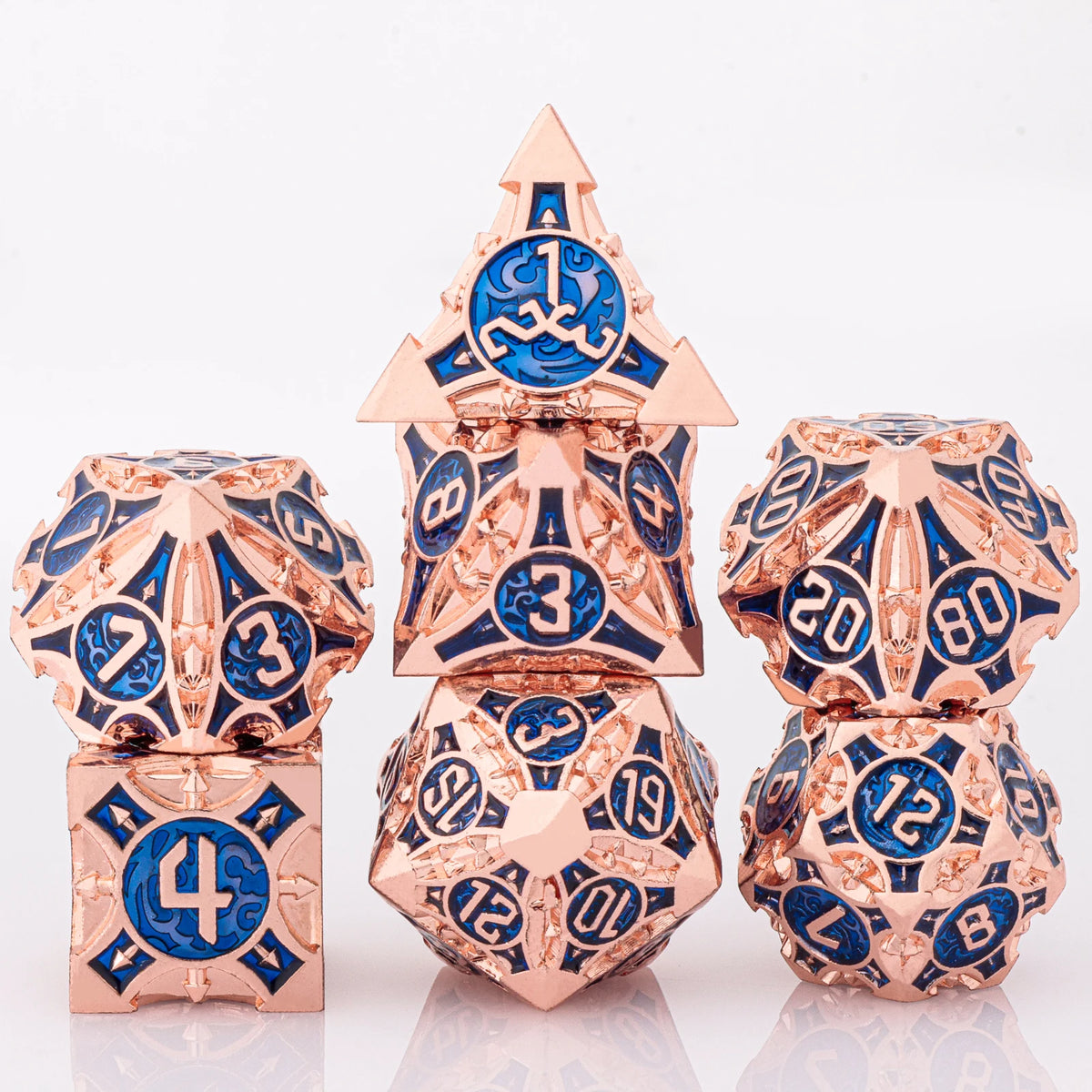 A set of seven metal dice featuring a skull and dragon design in rose gold and blue enamel.