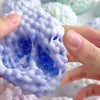 A hand is squeezing a light blue, textured squishy stress relief ball with visible air bubbles.