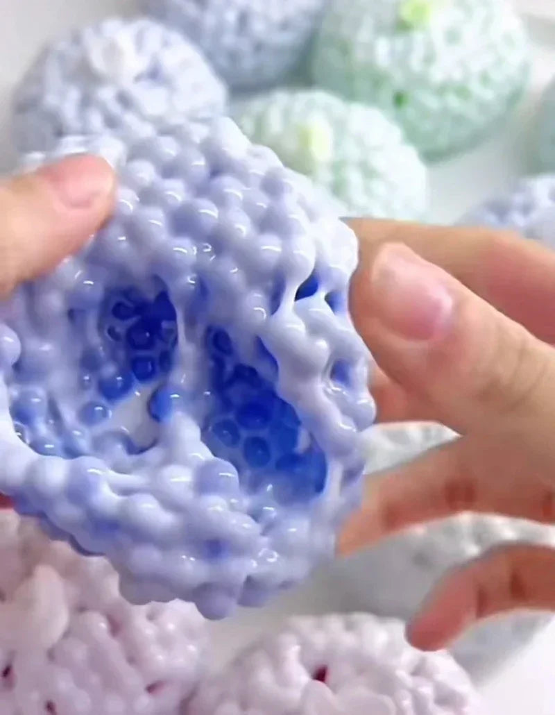 A hand is squeezing a light blue, textured squishy stress relief ball with visible air bubbles.