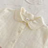 A close-up of a cream-colored baby cotton shirt with a collar and buttons.