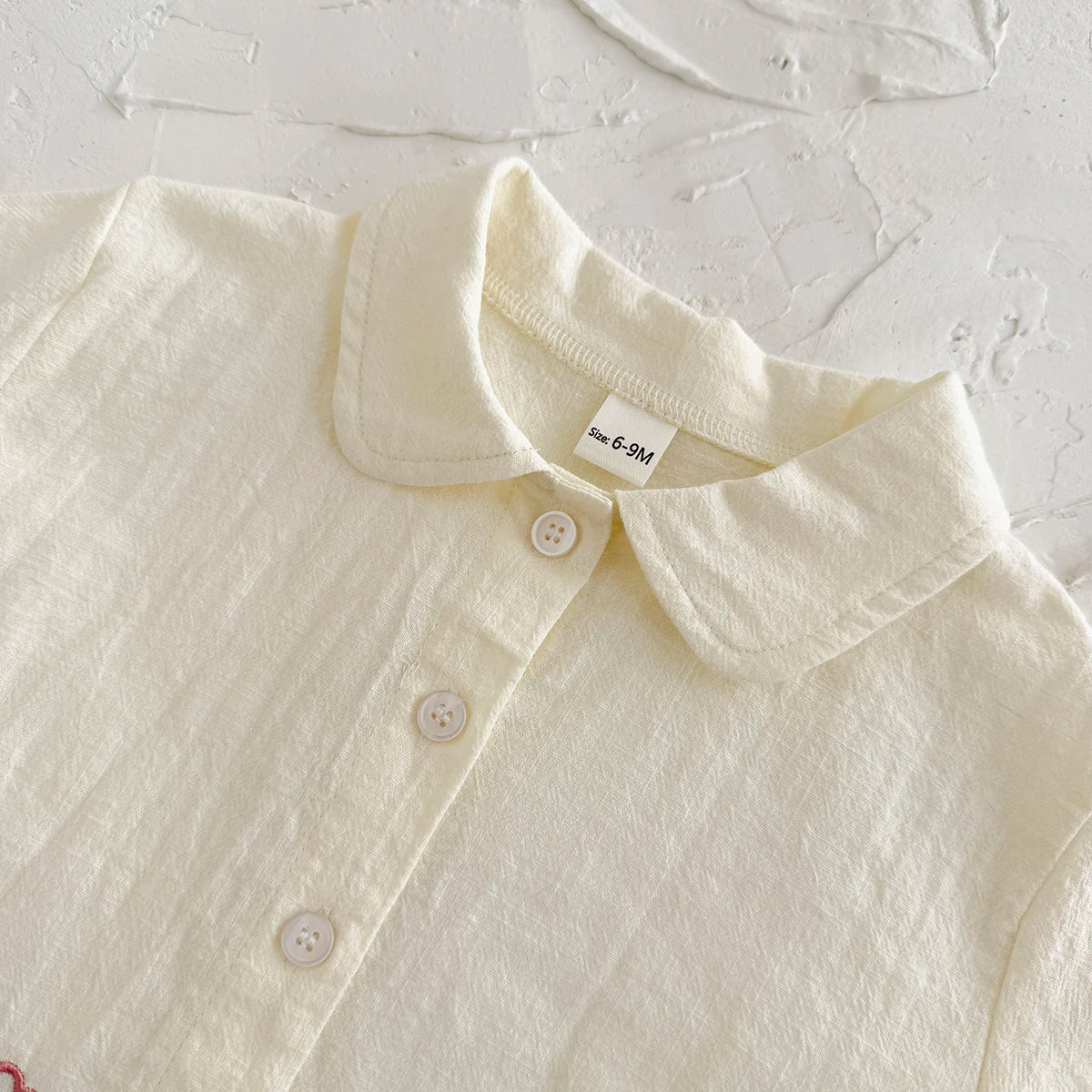 A close-up of a cream-colored baby cotton shirt with a collar and buttons.
