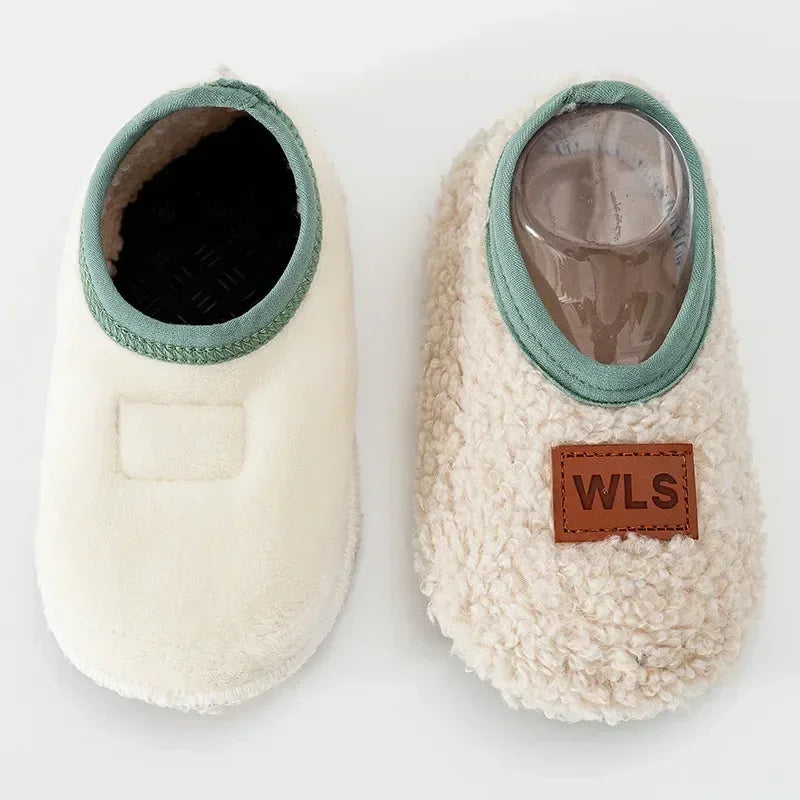 A pair of white plush baby slippers with a light green trim and a clear toe section.