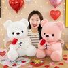 A woman holds a white teddy bear and a pink teddy bear, both holding red roses, on a wooden table.