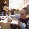 A woman is sealing a cardboard box with a marker, in the context of moving or shipping.