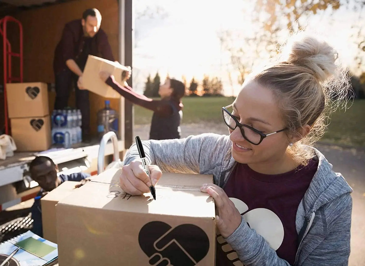 A woman is sealing a cardboard box with a marker, in the context of moving or shipping.