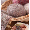 A close-up of soft, fuzzy alpaca blend yarn in various shades of gray and pink resting in a woven basket.