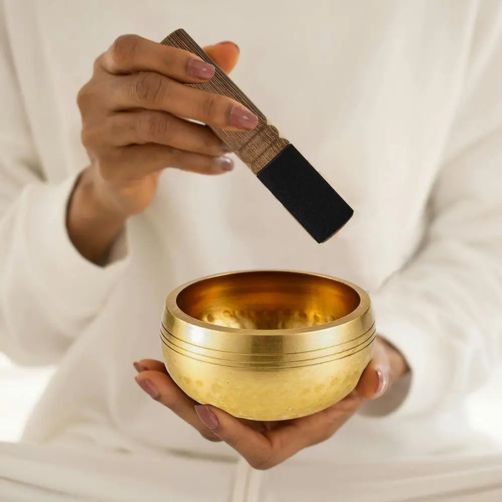 A hand holds a brass singing bowl and a wooden mallet, ready for meditation or yoga.