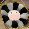 A large sunflower plush cushion with black and gray petals and a pink smiling face is displayed in a gold wire basket.