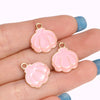 Two pink enamel marine life charms with gold-colored jump rings are displayed on a hand.