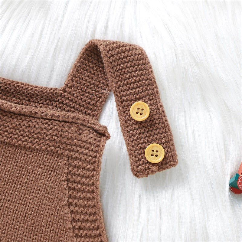 A brown knit romper with gold buttons is displayed on a white fluffy surface.