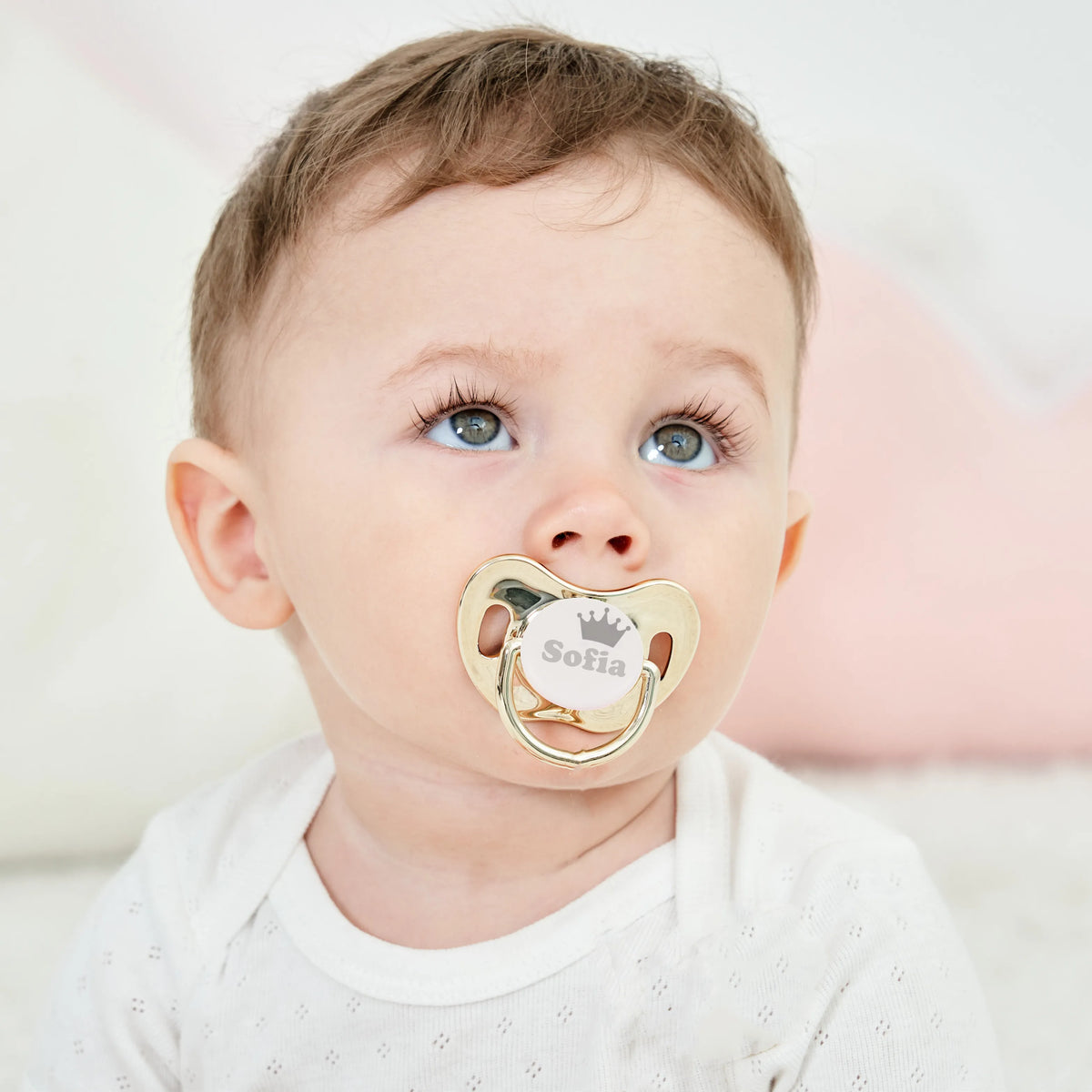 A baby wearing a personalized pacifier with a crown design and storage case.