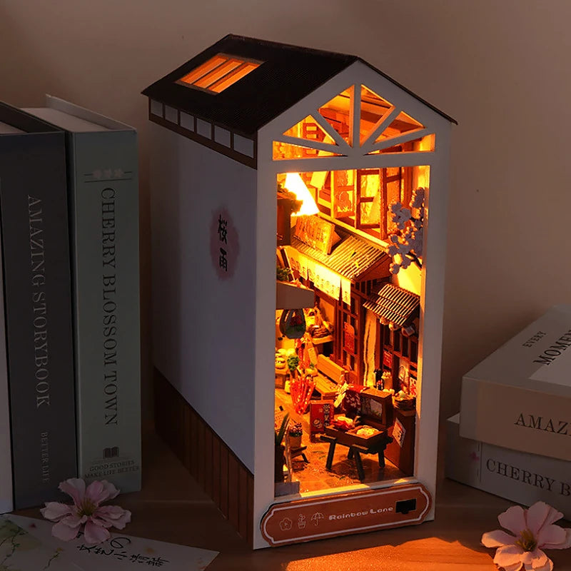 A miniature wooden dollhouse kit with furniture displayed in a lighted display box.