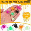 A hand holds various plastic mini fake black spiders in bright colors including orange, pink, and green.
